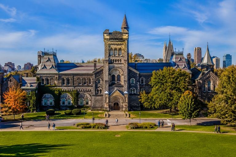 A university campus in Canada, stone buildings with autumn trees along a paved forecourt.